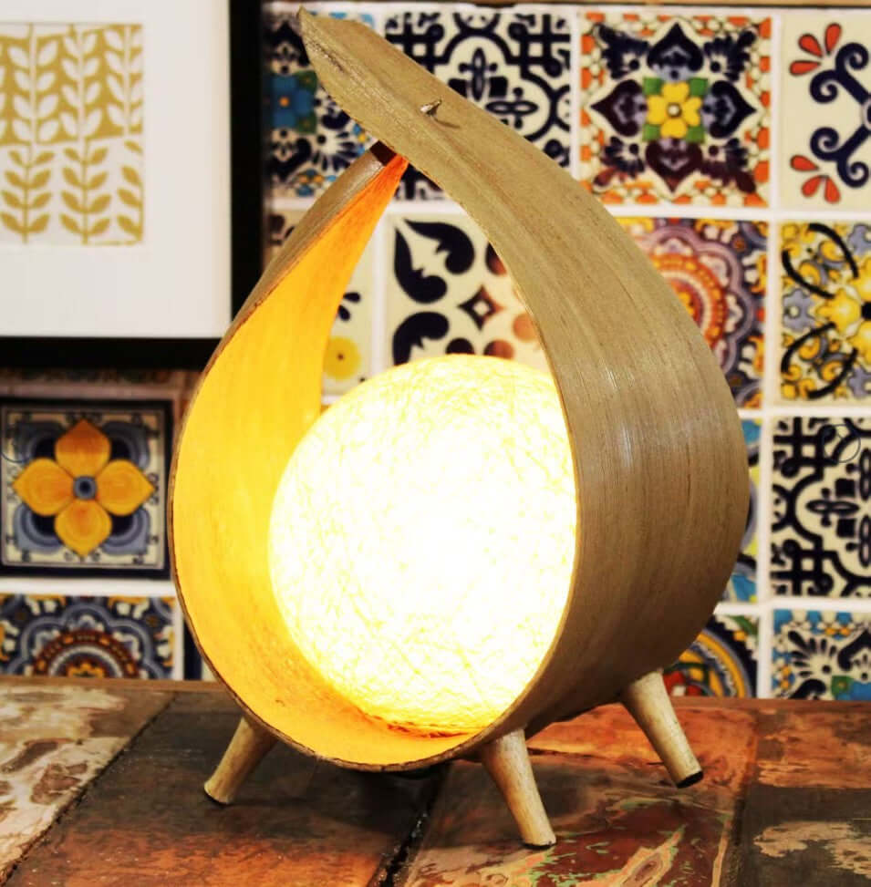 Wooden lamp with a glowing interior on a wooden surface with a colorful tile pattern in the background.