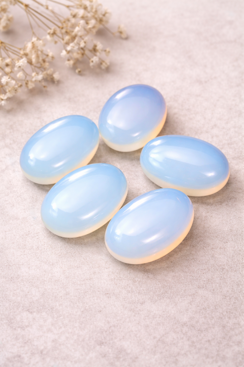 Five light blue stones on a textured beige surface with dried flowers.