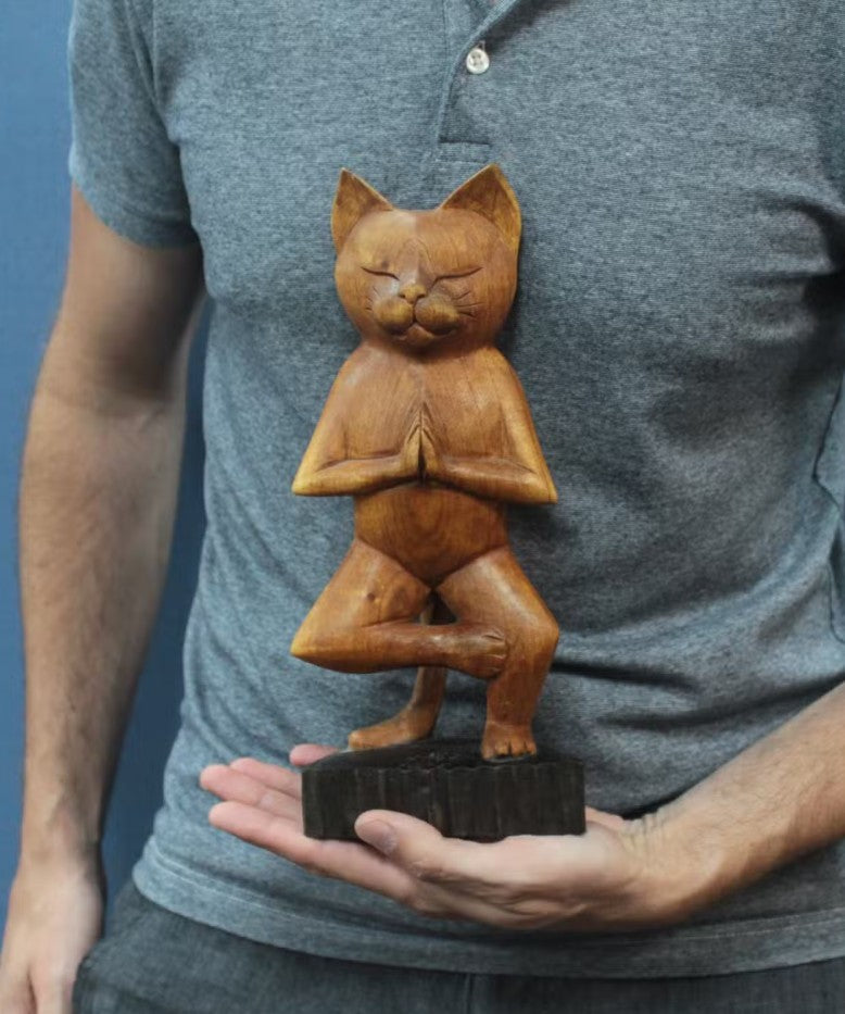 Wooden sculpture of a cat in a yoga pose held by a person wearing a gray shirt.
