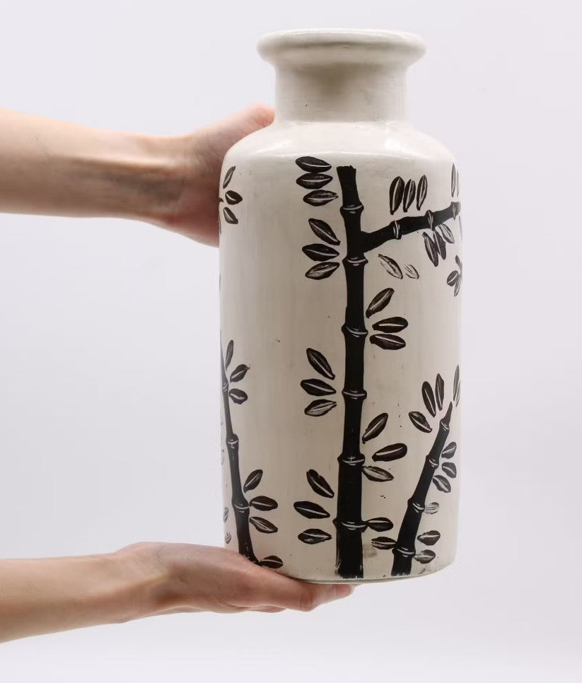 Ceramic vase with black tree design held by a hand against a white background